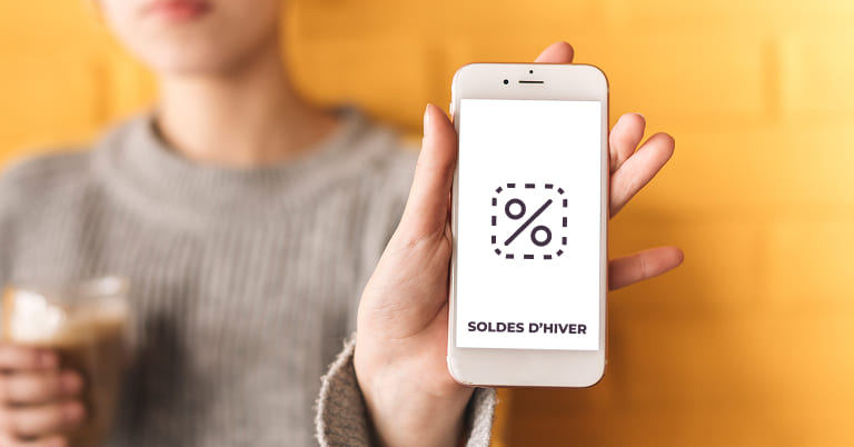 femme tenant un téléphone avec un % pour imager les soldes d'hiver 2026